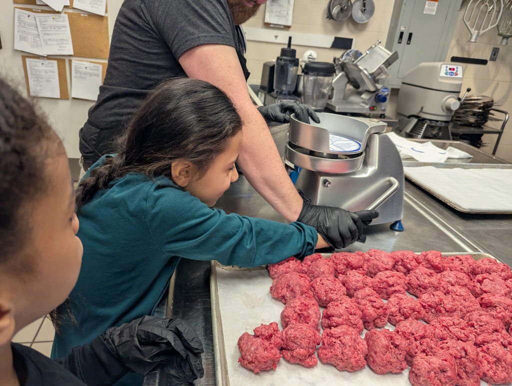 A student wearing a teal shirt is helping press meat to make it into a patty for burgers. 
