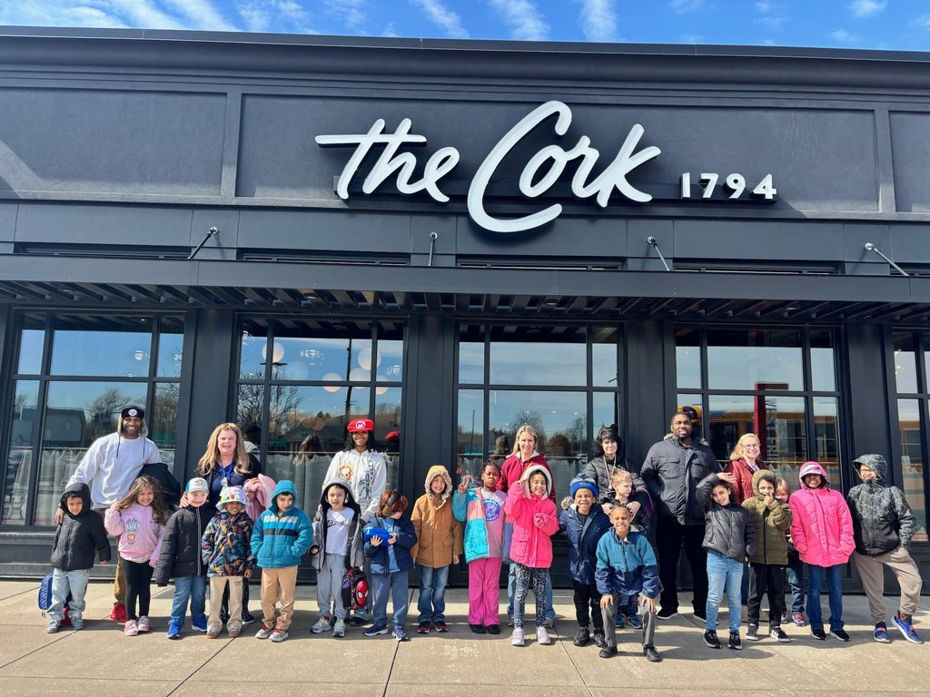 Students and staff are wearing jackets and standing in front of the Cork restaurant. 