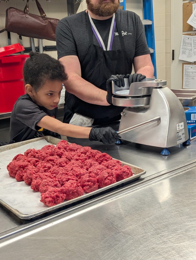 A student wearing a black shirt is helping press meat to make it into a patty for burgers. 