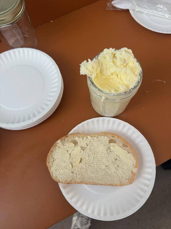 Bread on a plate with butter spread on the bread and a jar of butter next to it on a table. 