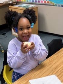 A young girl is wearing a purple shirt and eating bread with butter on it. 