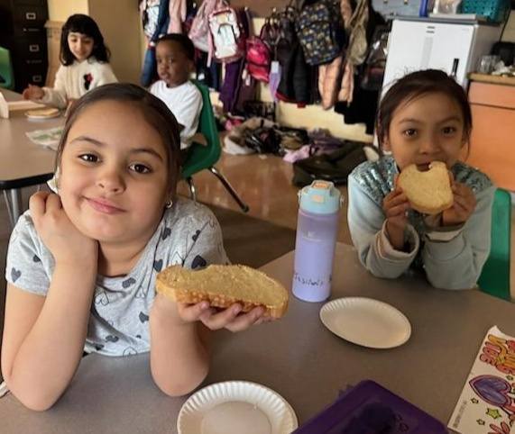A young girl is holding her bread with butter on it while the girl next to her is eating bread with butter on it. 