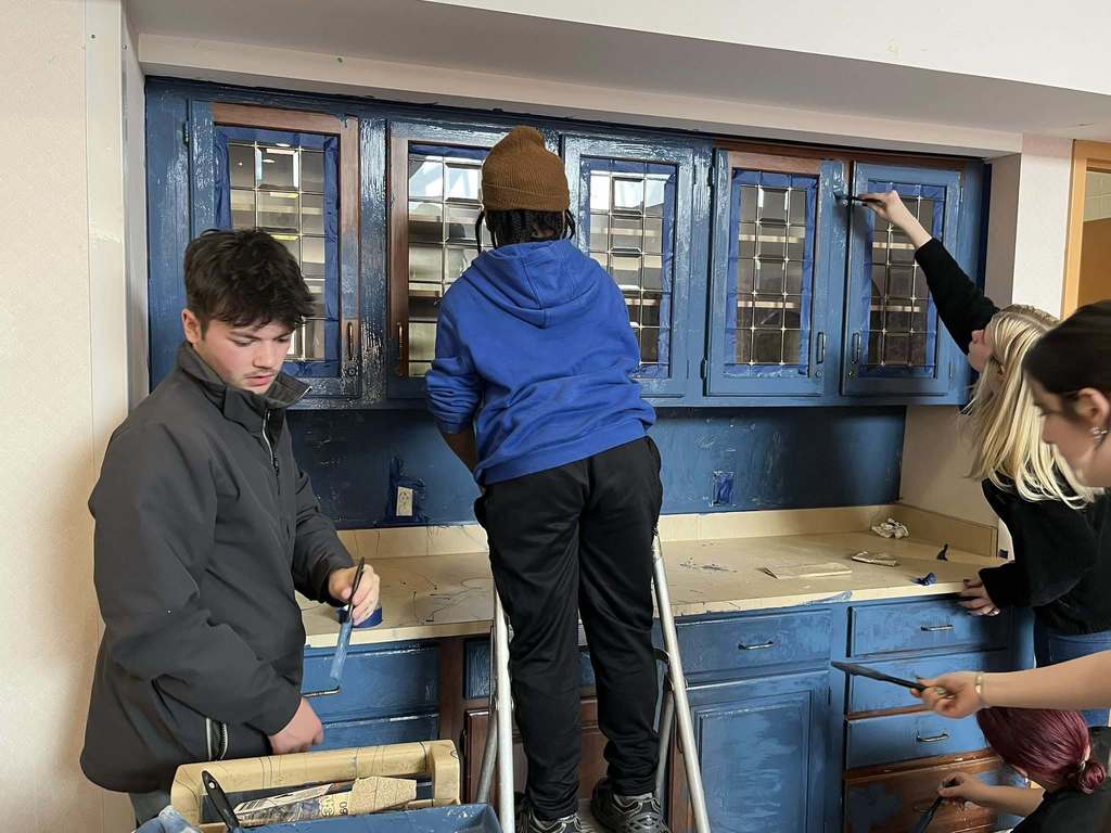 Students paint a brown cabinet to now be blue. 