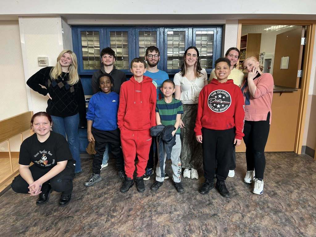 Students standing and smiling in front of the blue cabinet they painted. 