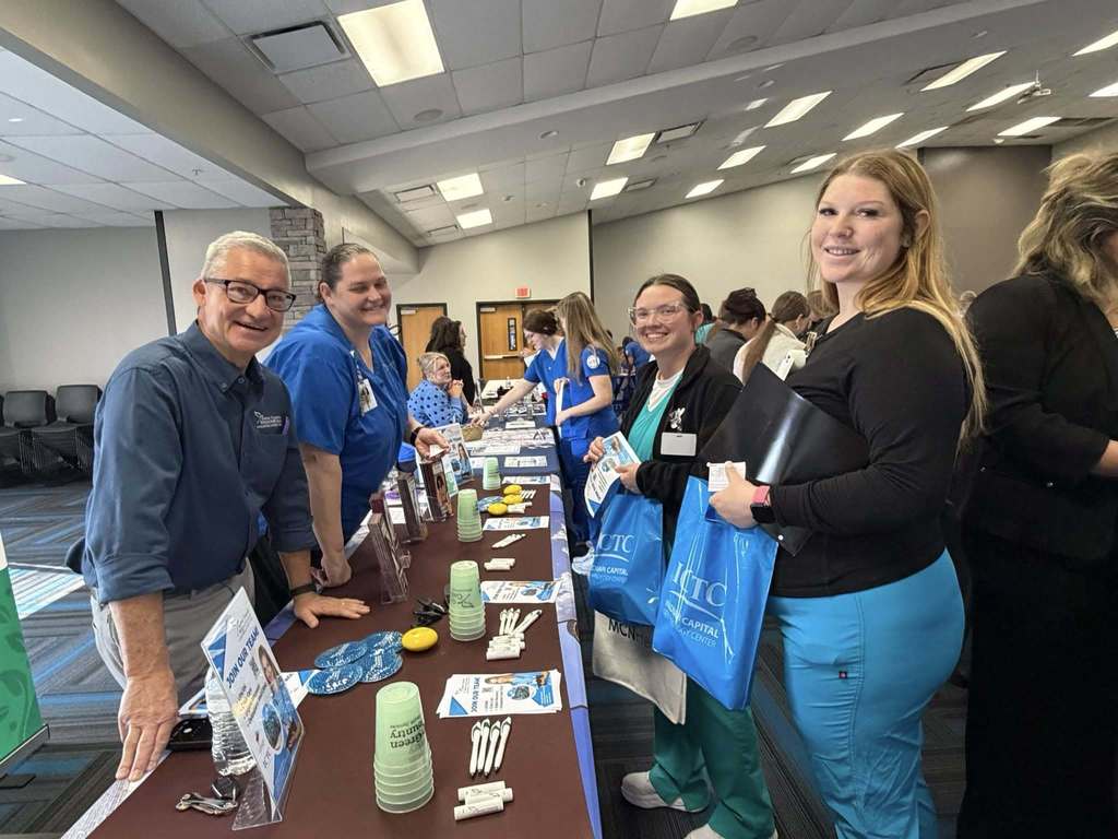 Five people gather around a table with promotional materials in a conference room with fluorescent lighting.
