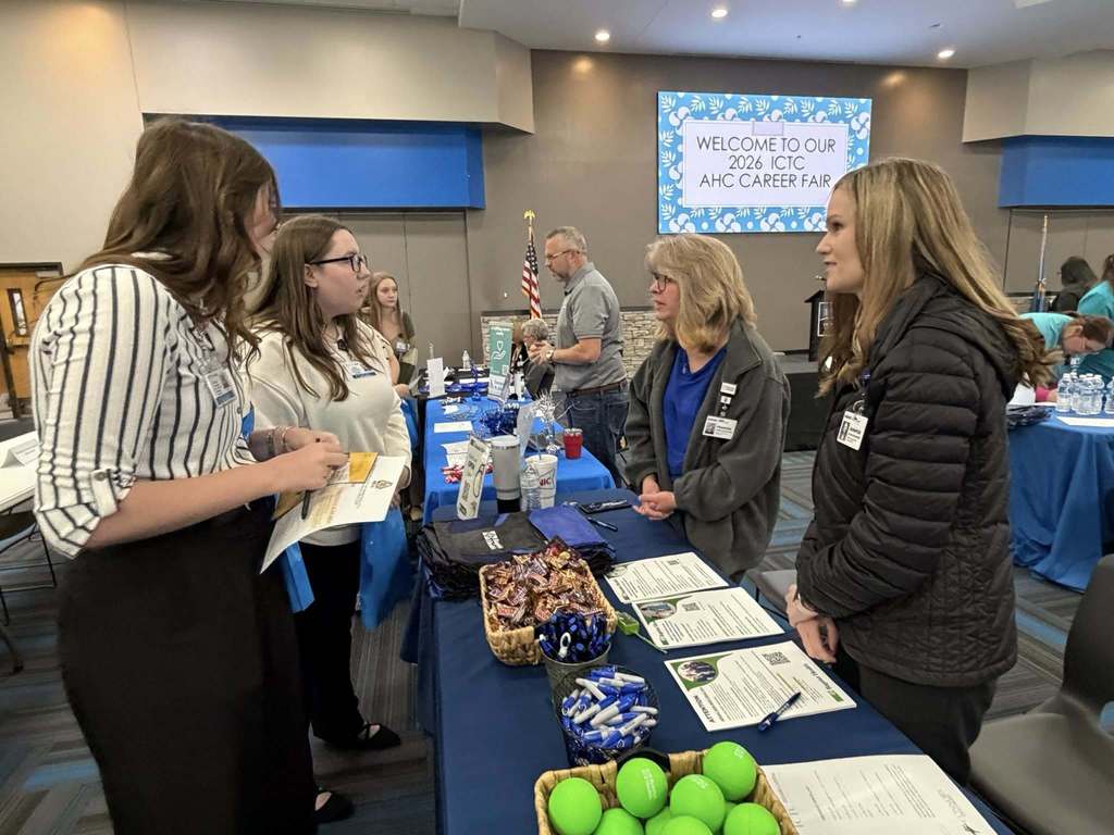 A group of women at a table with brochures, a bowl of tennis balls, and other items.