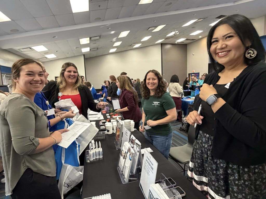 Four women stand around a table with various items. They appear to be at an event.