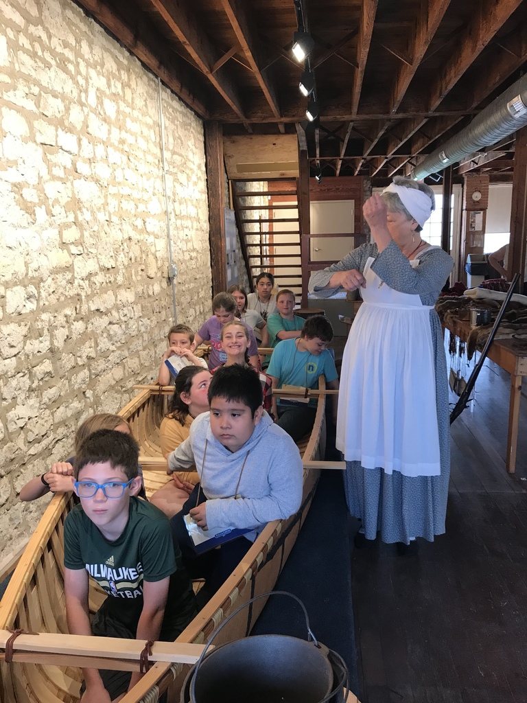 students sitting in an old birch bark canoe as someone tells them about it