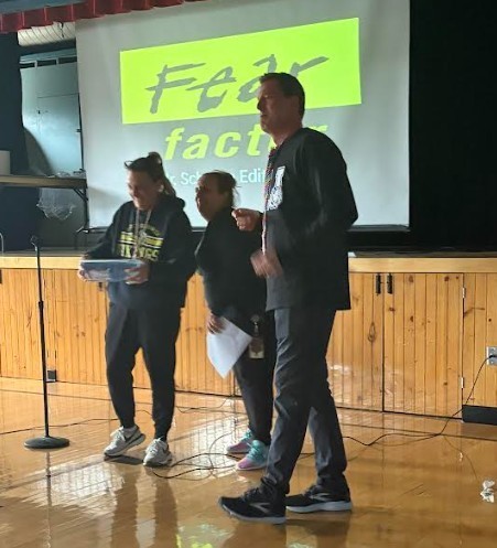 Three people stand on a stage with a projection screen behind them, displaying a yellow text.