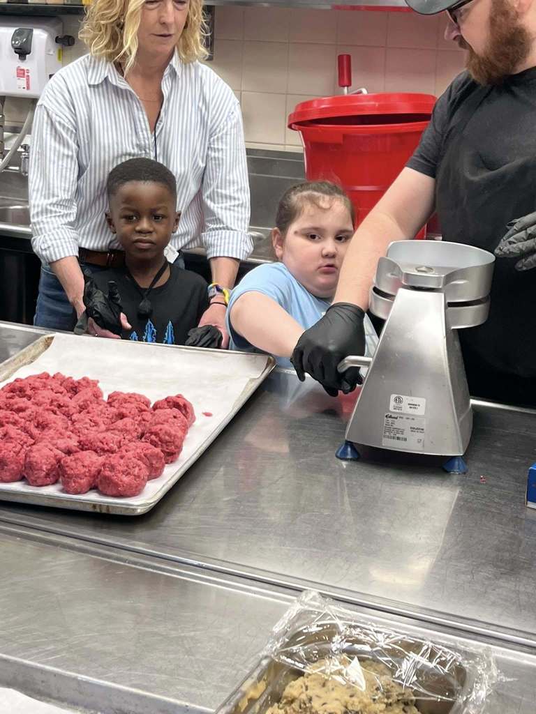 Students helping press meat to make it into a burger. 