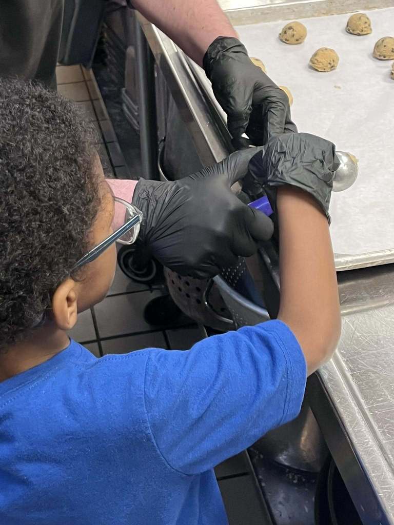 A student wearing gloves and helping make cookies at the restaurant. 