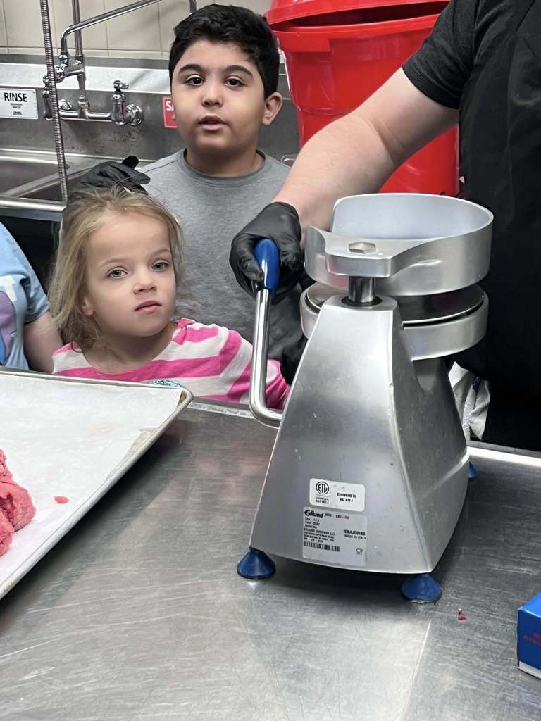 Students helping press meat to make it into a burger. 