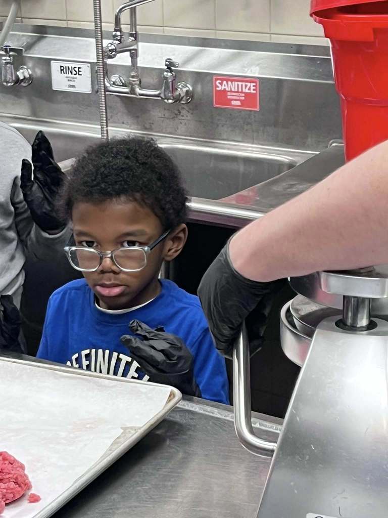 Student wearing gloves and looking at the meat in the restaurants kitchen. 