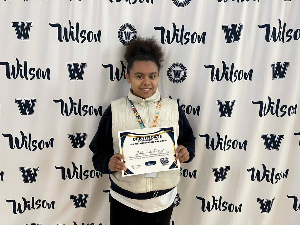 A student in a black long shirt and white vest on top is holding their certificate. 