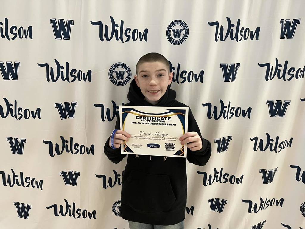 A student in a black hoodie is holding their certificate. 