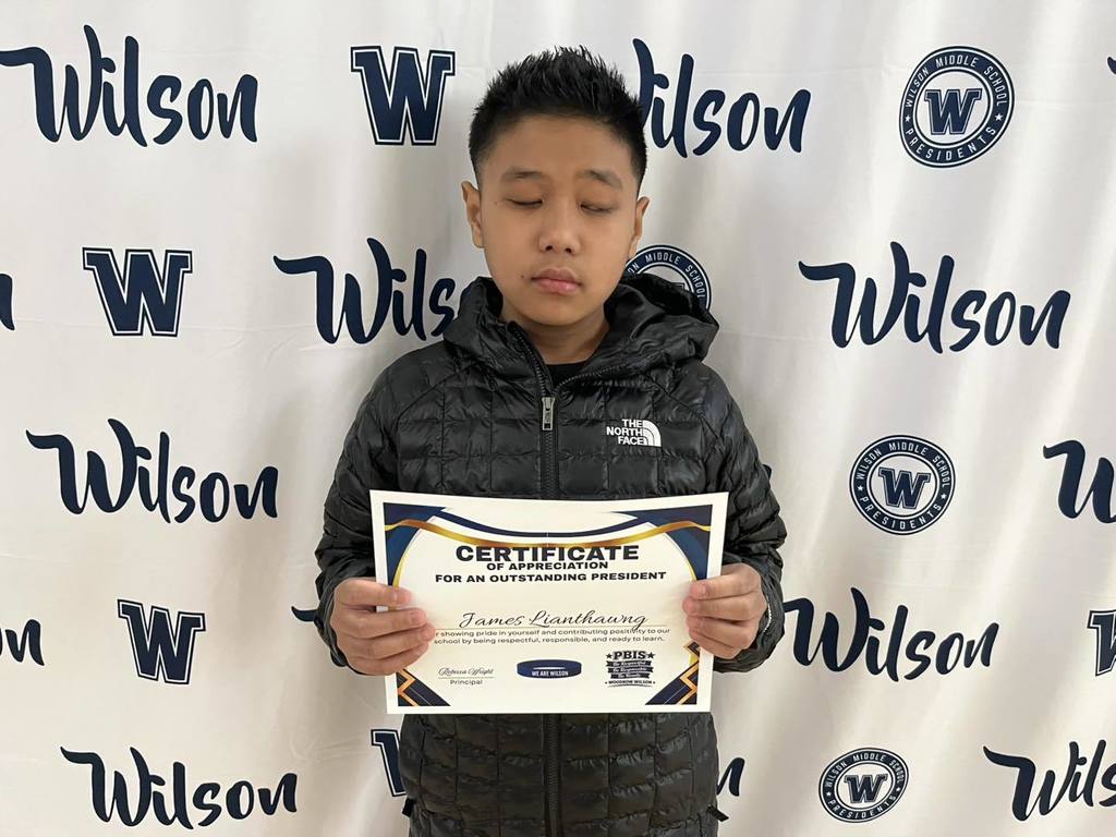 A student in a black jacket is holding his certificate. 