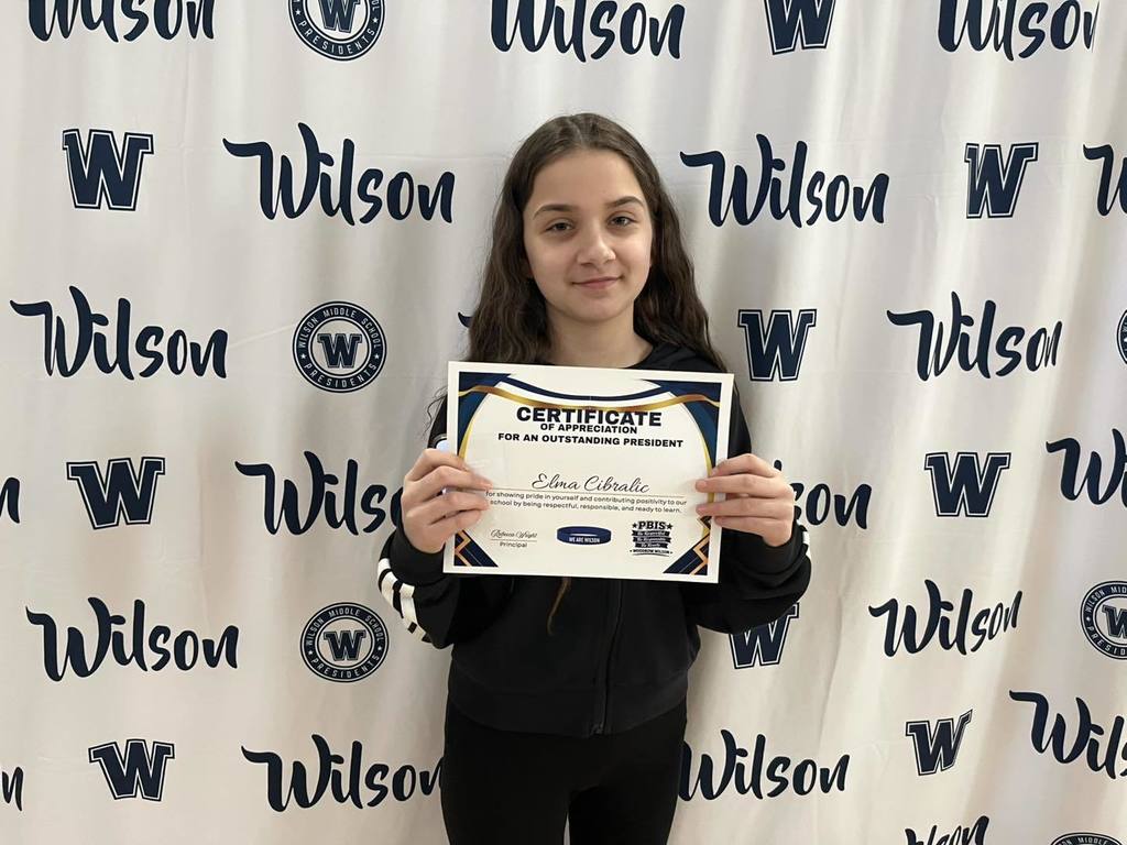 A student in a black outfit is holding their certificate. 