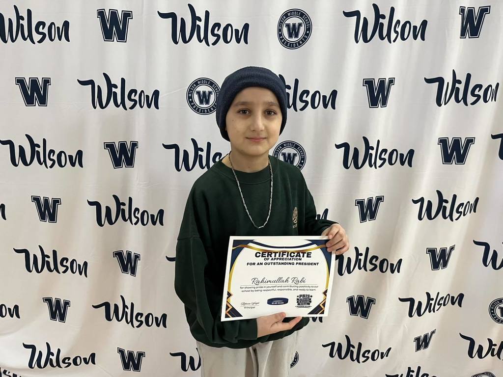 A student in a green shirt is holding their certificate. 