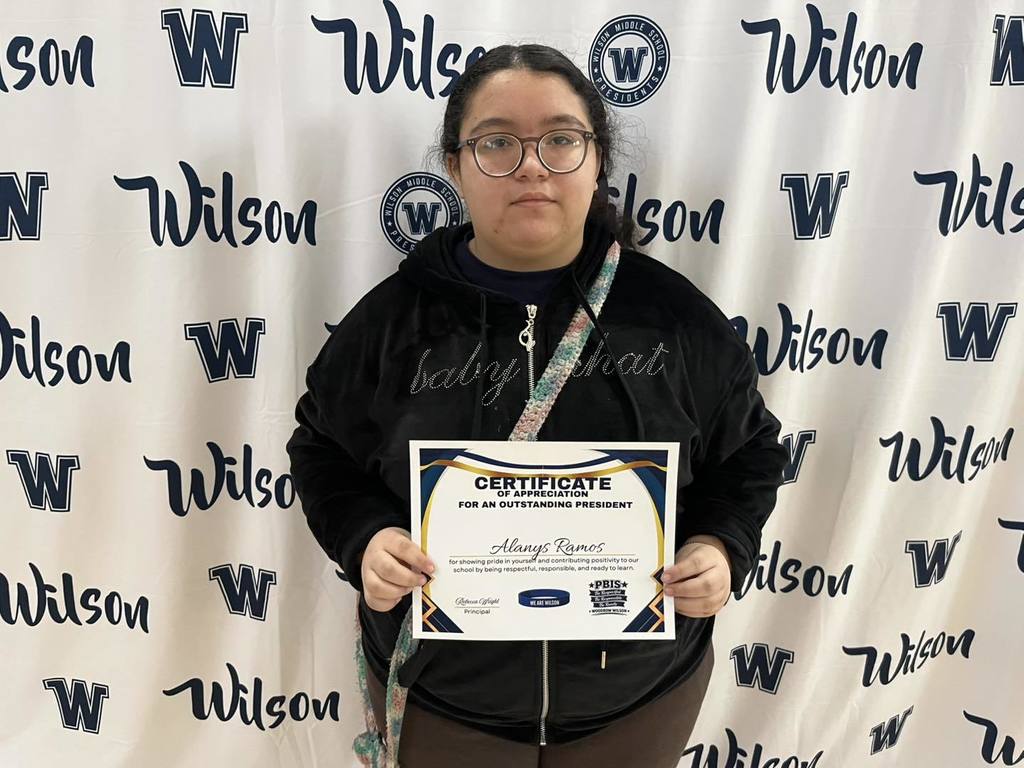 A student in a black hoodie is holding their certificate. 