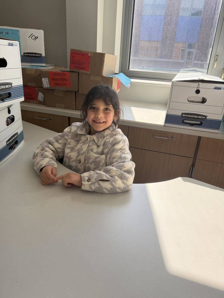 A young girl sitting at a desk in her new classroom. 
