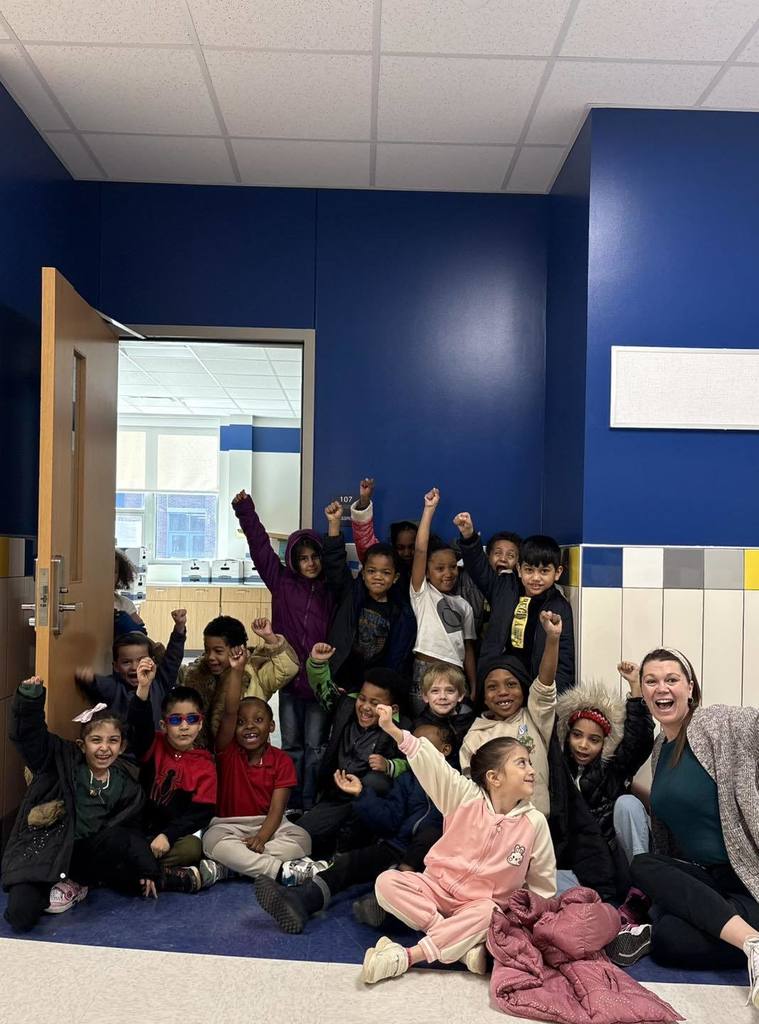 Students and teacher cheering while sitting in front of their new classroom in the New Edison Elementary Building. 