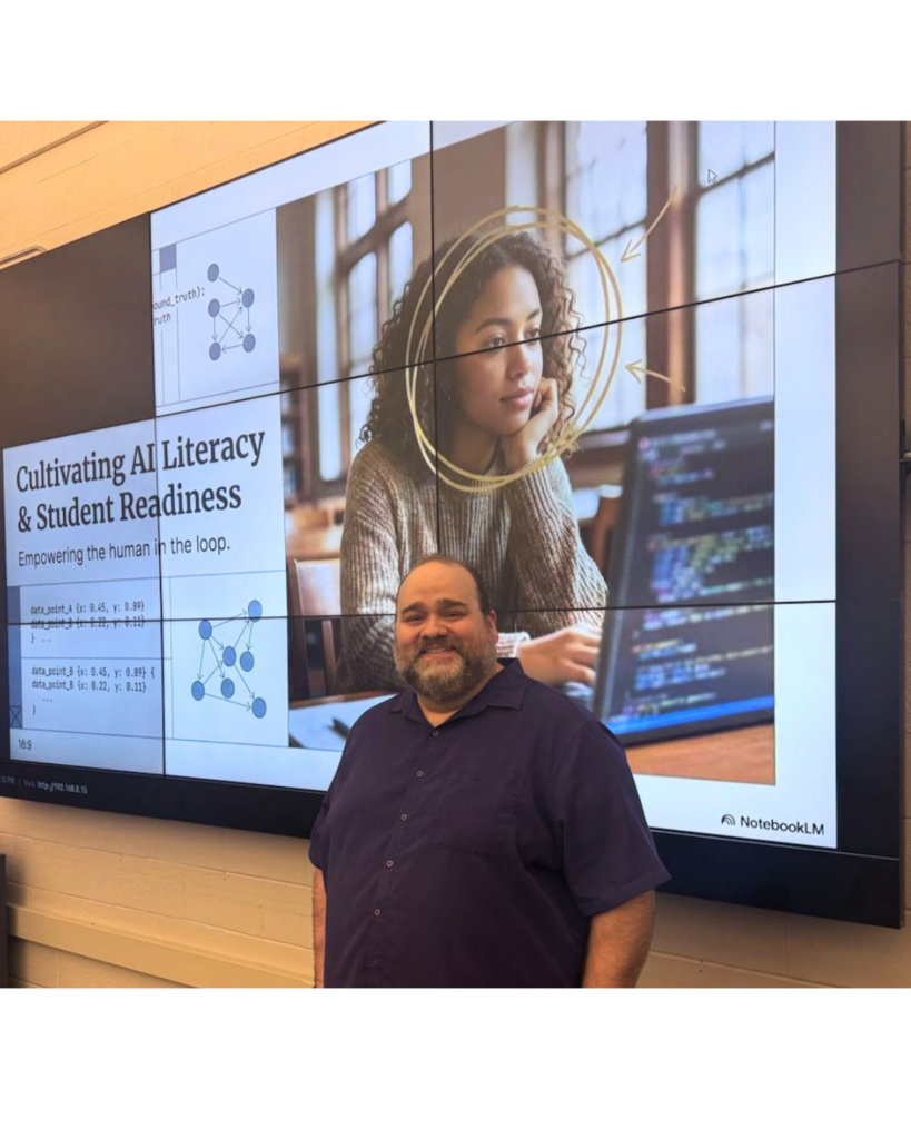 A presenter stands in front of a large wall-mounted screen displaying a slide titled “Cultivating AI Literacy & Student Readiness,” with graphics of connected nodes and a photo of a student working on a laptop with code visible on the screen.