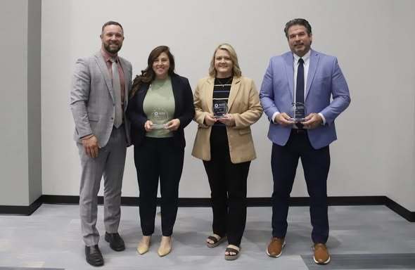 Four individuals, two men and two women, dressed in business attire, standing together holding awards.