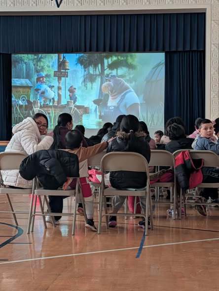 Students sitting on chairs and watching a movie on a big screen.