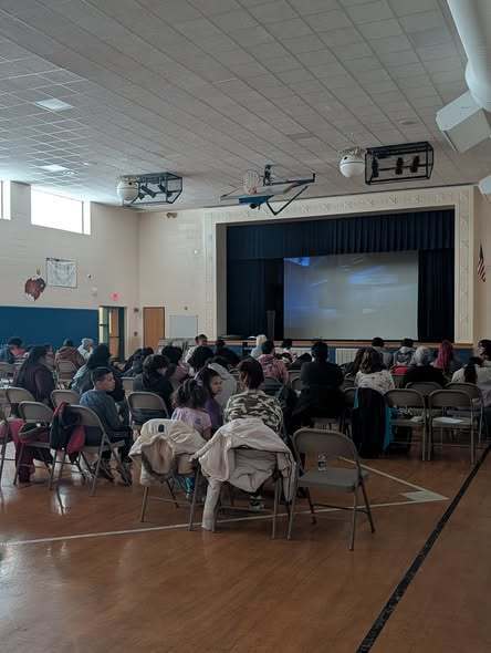 Students and families sitting on chairs and watching a movie on a big screen.