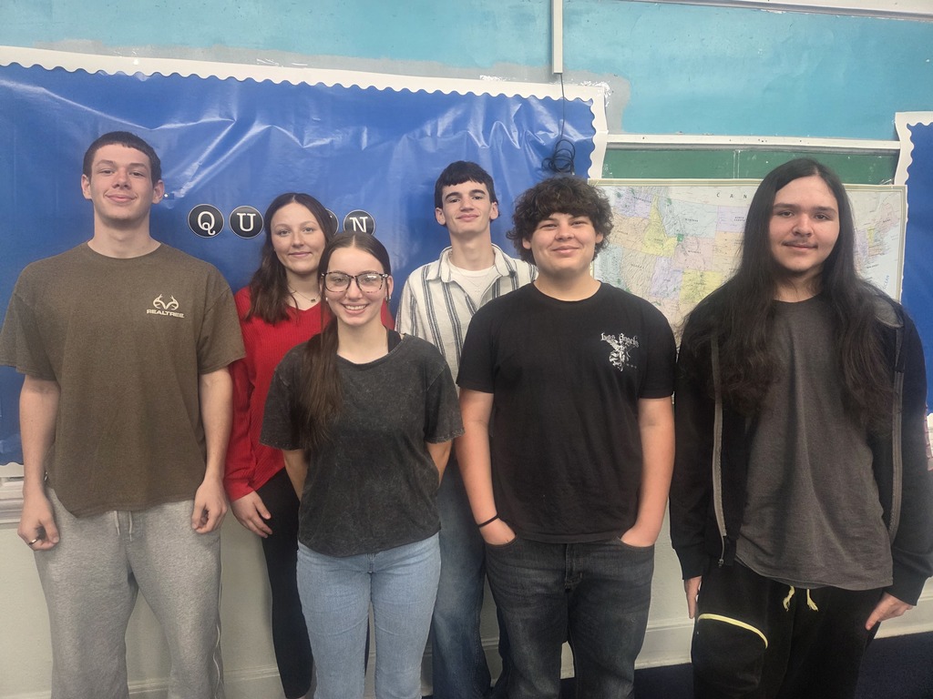 A group of six people, including three women and three men, stands close together against a blue background.