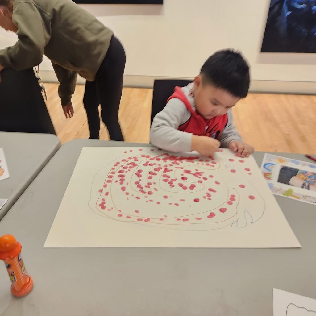 A kid coloring red dots on a large paper. 