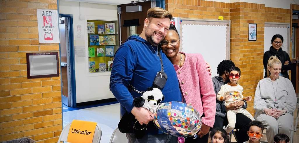 A man and woman stand together holding a colorful balloon. They are surrounded by a group of people.