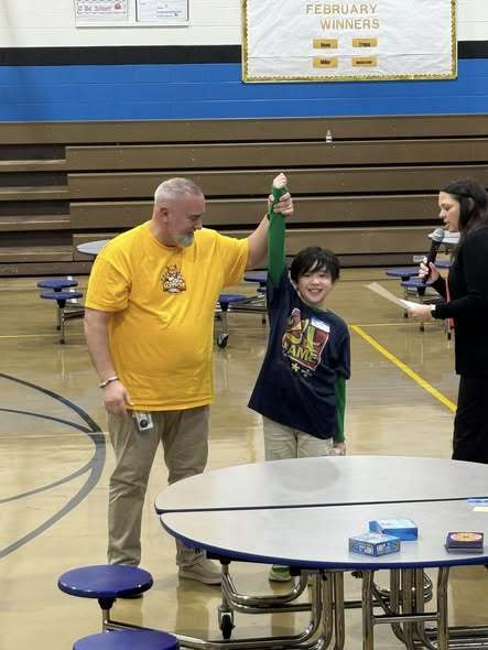 A man in a yellow shirt holding up the hand of the student who won.