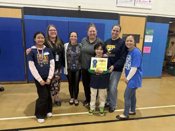 Staff and parents standing next to the two finalists while one holds their certificate. 