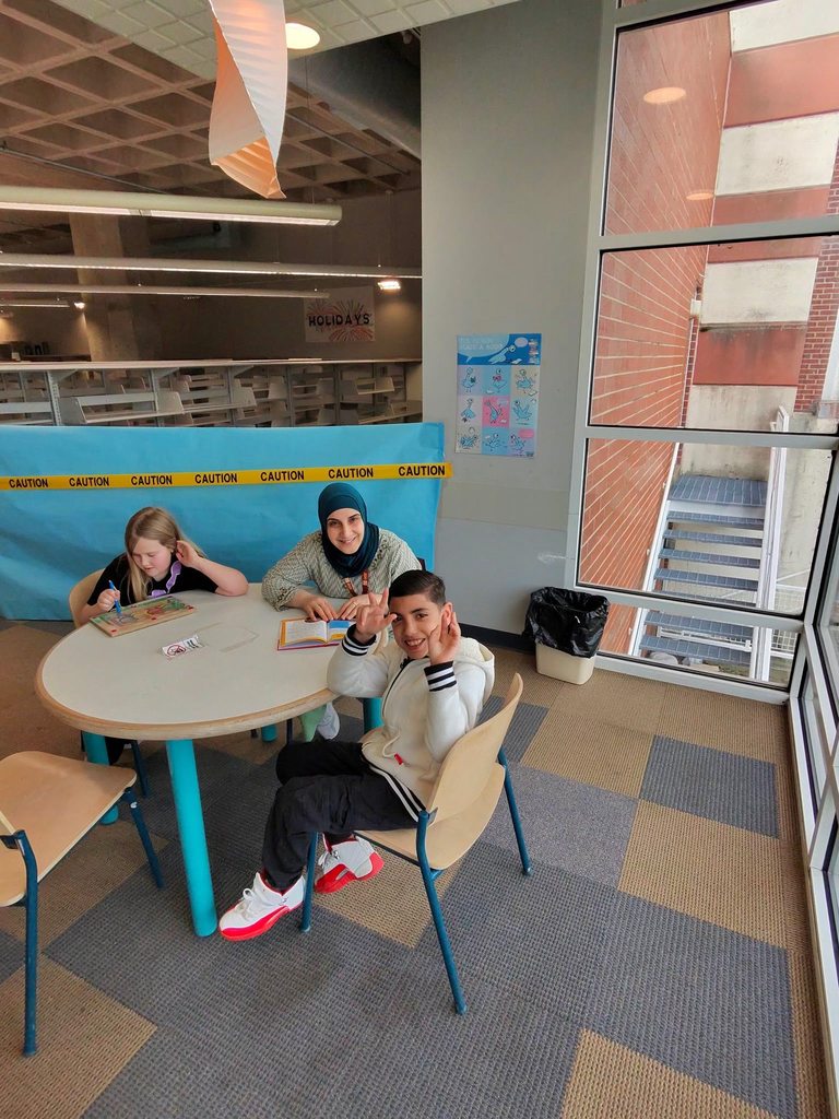 Young boy and staff member are sitting at a circular table withy a young girl who is playing an activity and the boy and staff member are posing for a photo. 