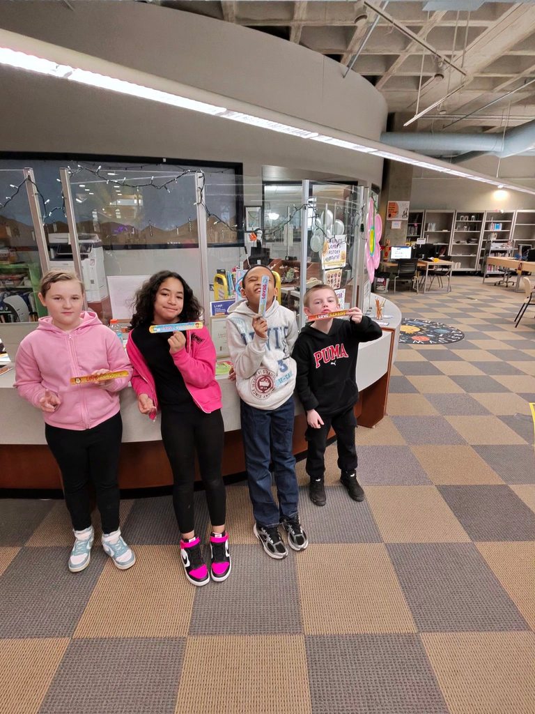 Kids holding books marks in their hands and are posing for a photo in the children's library. 