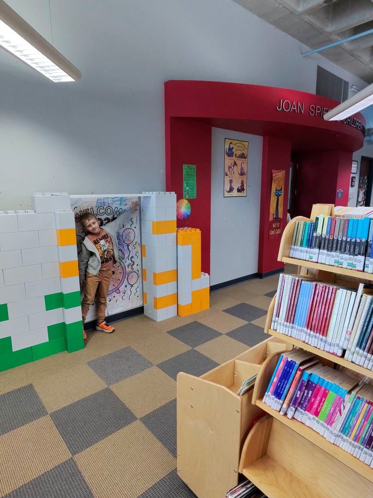 A young boy is posing in a Lego arch that is located in the children's library.