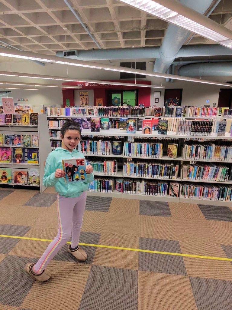 A young girl posing for a picture while holding a book in the children's library. 