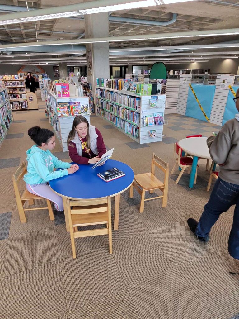 A women reading to a young girl at a circular table in the children's library. 