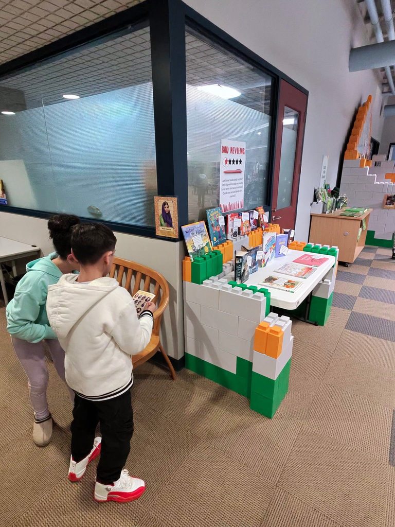 Kids are looking at a paper and standing in the children library. 