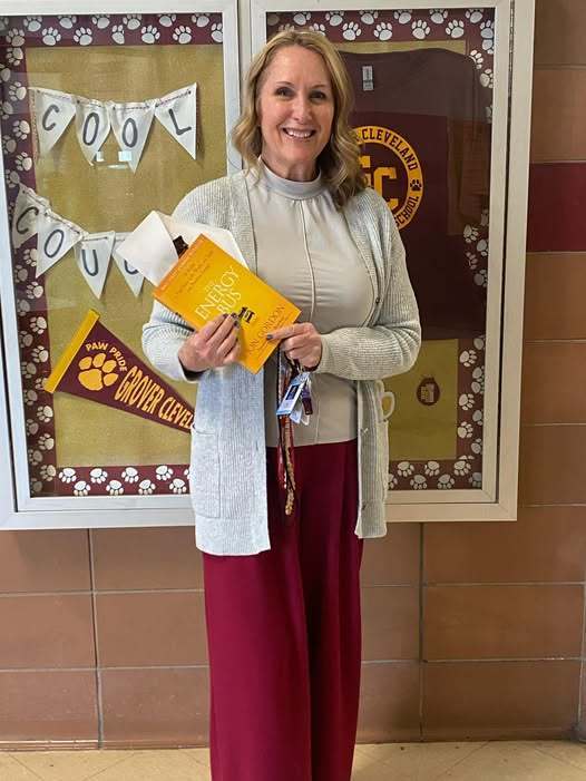 AA women who is wearing red pants is holding a yellow book in the Grover Cleveland hall. 