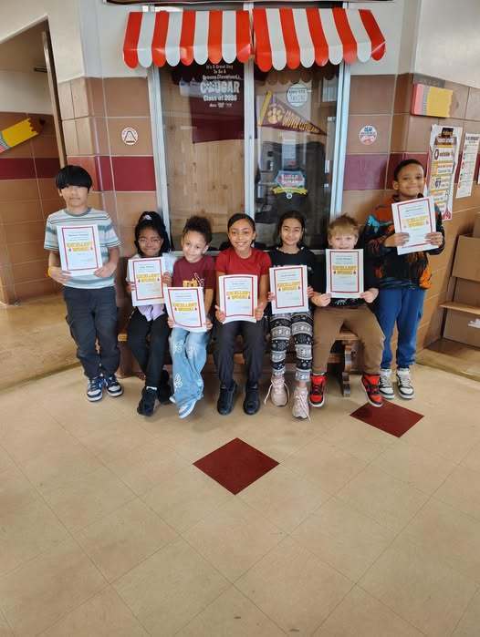 Kids sitting on a bench and two kids on each end are standing while they all hold their Cool Cougars awards for the 3rd quarter.