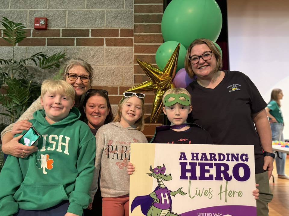 Family standing next to their child who has a green is holding a sign that says "A Harding Hero Lives Here" on it. 