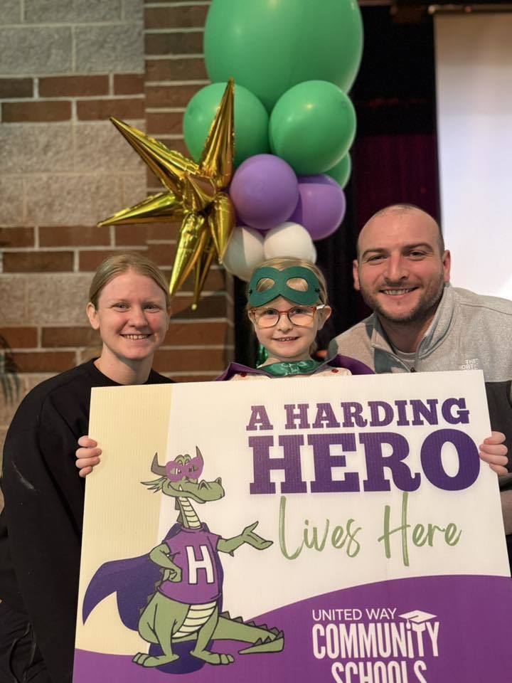 Parents standing next to their child who has a green is holding a sign that says "A Harding Hero Lives Here" on it. 