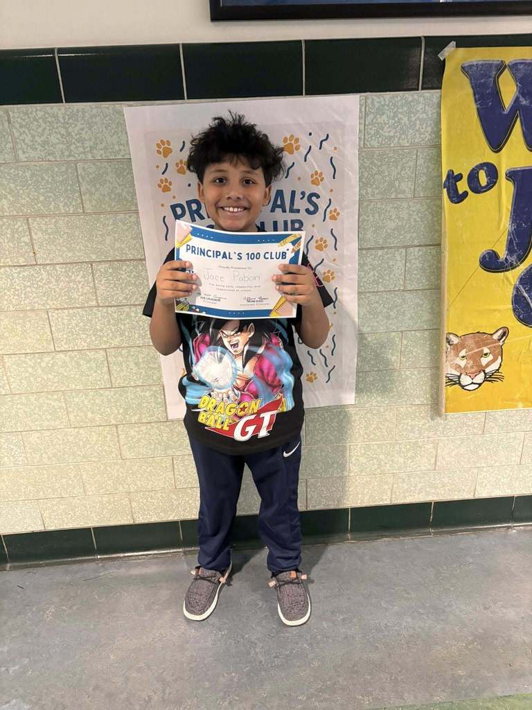 Young boy wearing a graphic black shirt is holding his "Principal 100 Club" Certificate. 