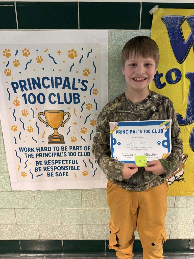 Young boy wearing a camouflage shirt is holding his "Principal 100 Club" Certificate. 