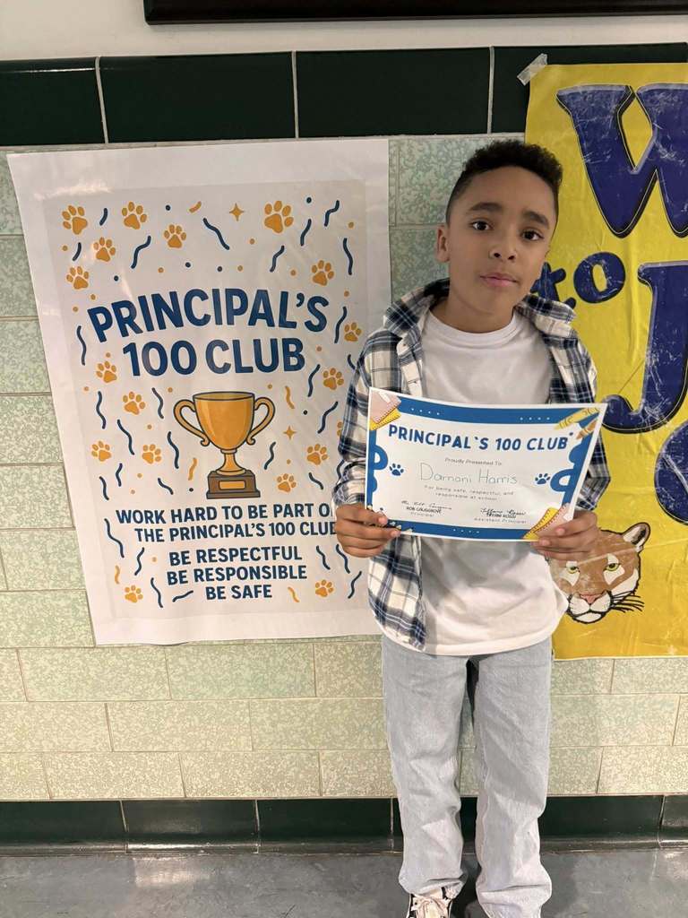 Young boy wearing a white shirt and plaid jacket is holding his "Principal 100 Club" Certificate. 