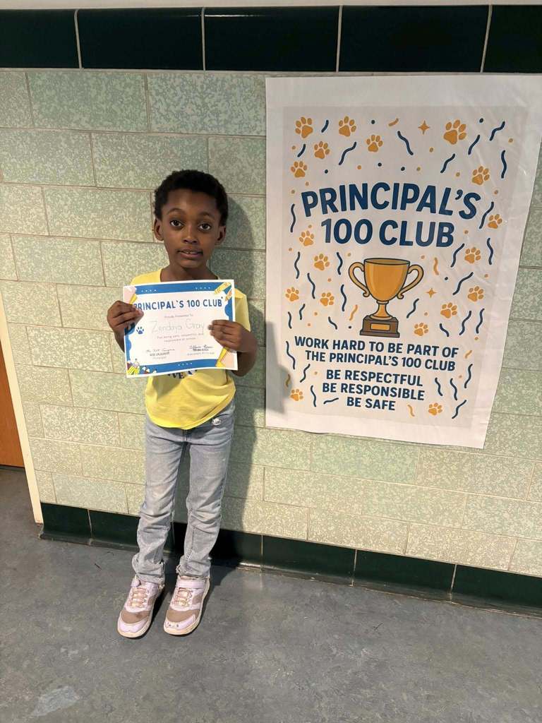 Young boy wearing a yellow shirt is holding his "Principal 100 Club" Certificate. 