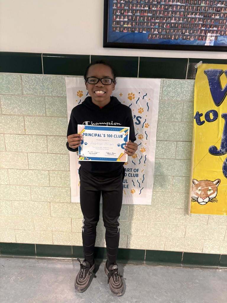 Young boy wearing a black hoodie is holding his "Principal 100 Club" Certificate. 