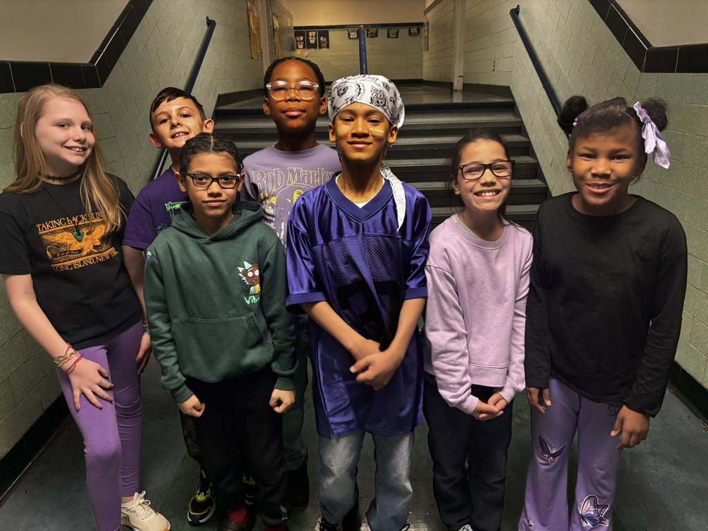 Students wearing purple and smiling in the school hall. 